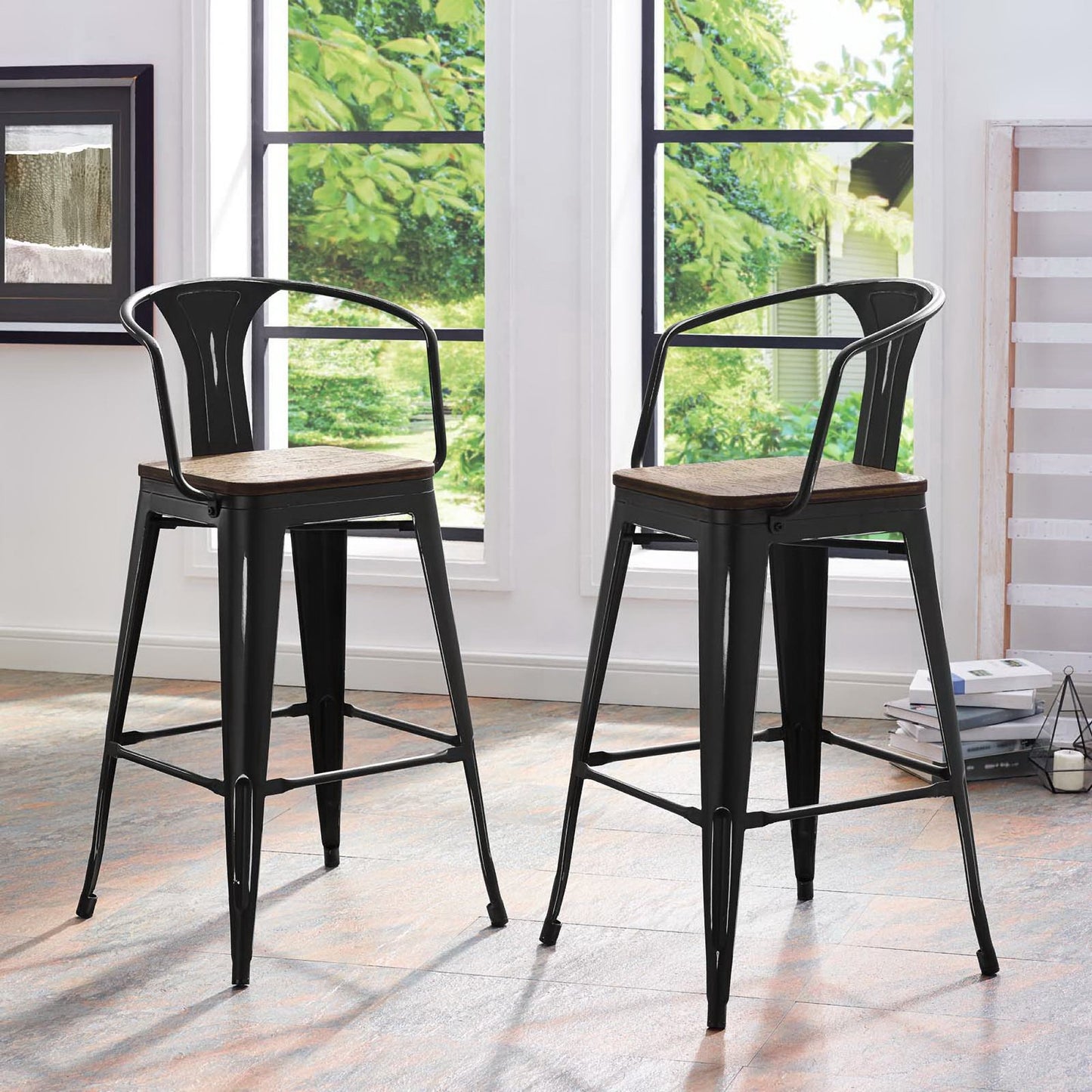 Two black metal bar stools with wooden seats & curved backs, tall tapered legs, in a bright room by wide windows.