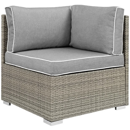 Gray outdoor wicker corner seating unit with thick cushioned seat and two back cushions, white piping.
