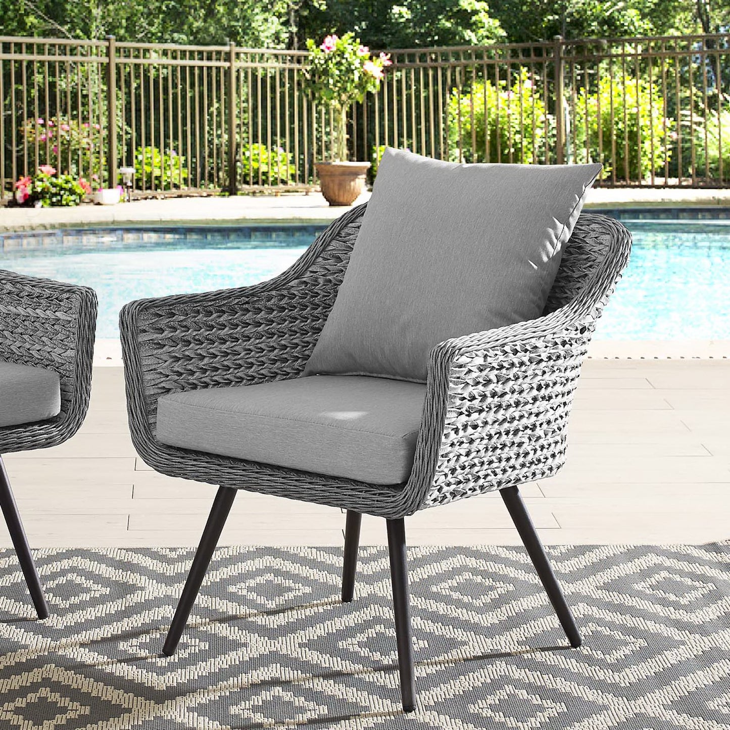 Gray wicker outdoor armchair with light gray cushions, poolside on a geometric rug.