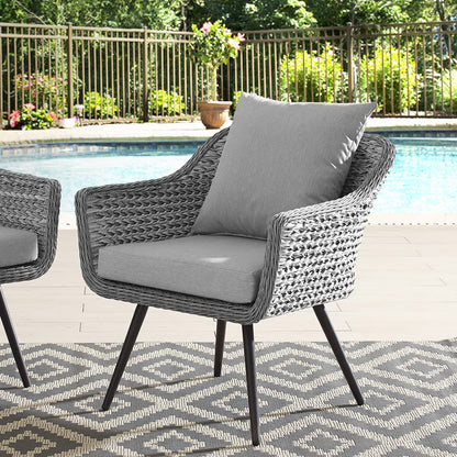 Gray wicker outdoor armchair with light gray cushions, poolside on a geometric rug.