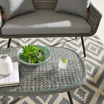 Round glass-top wicker coffee table with a succulent bowl on a geometric gray-beige outdoor rug.