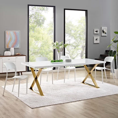 White rectangular dining table with gold X-frame legs by large windows.
