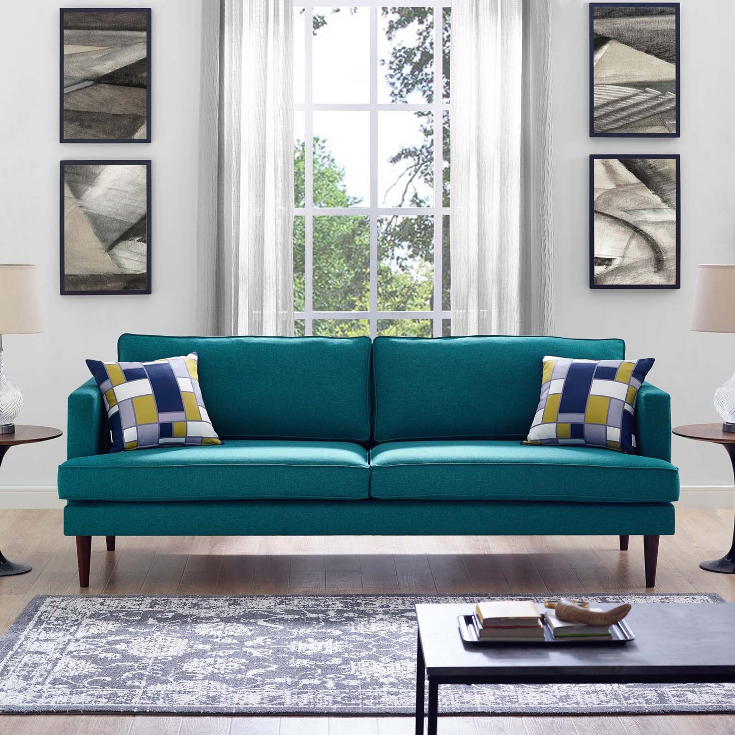 Teal mid-century sofa with tapered legs, two yellow-blue geometric cushions, in a bright living room with a large window.