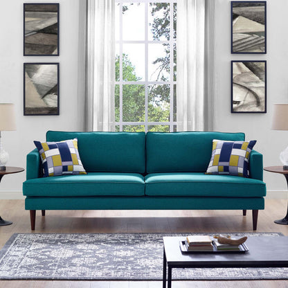 Teal mid-century sofa with tapered legs, two yellow-blue geometric cushions, in a bright living room with a large window.