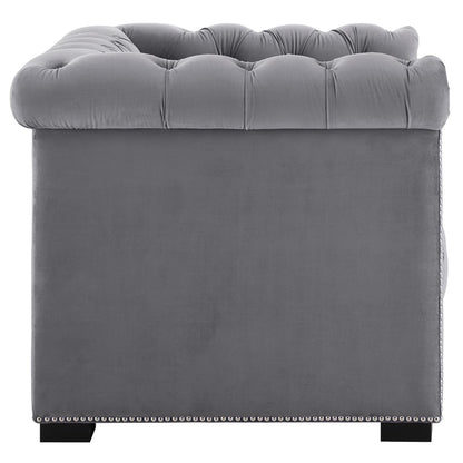 Gray velvet tufted back of an armchair with nailhead trim along the base and dark block feet.