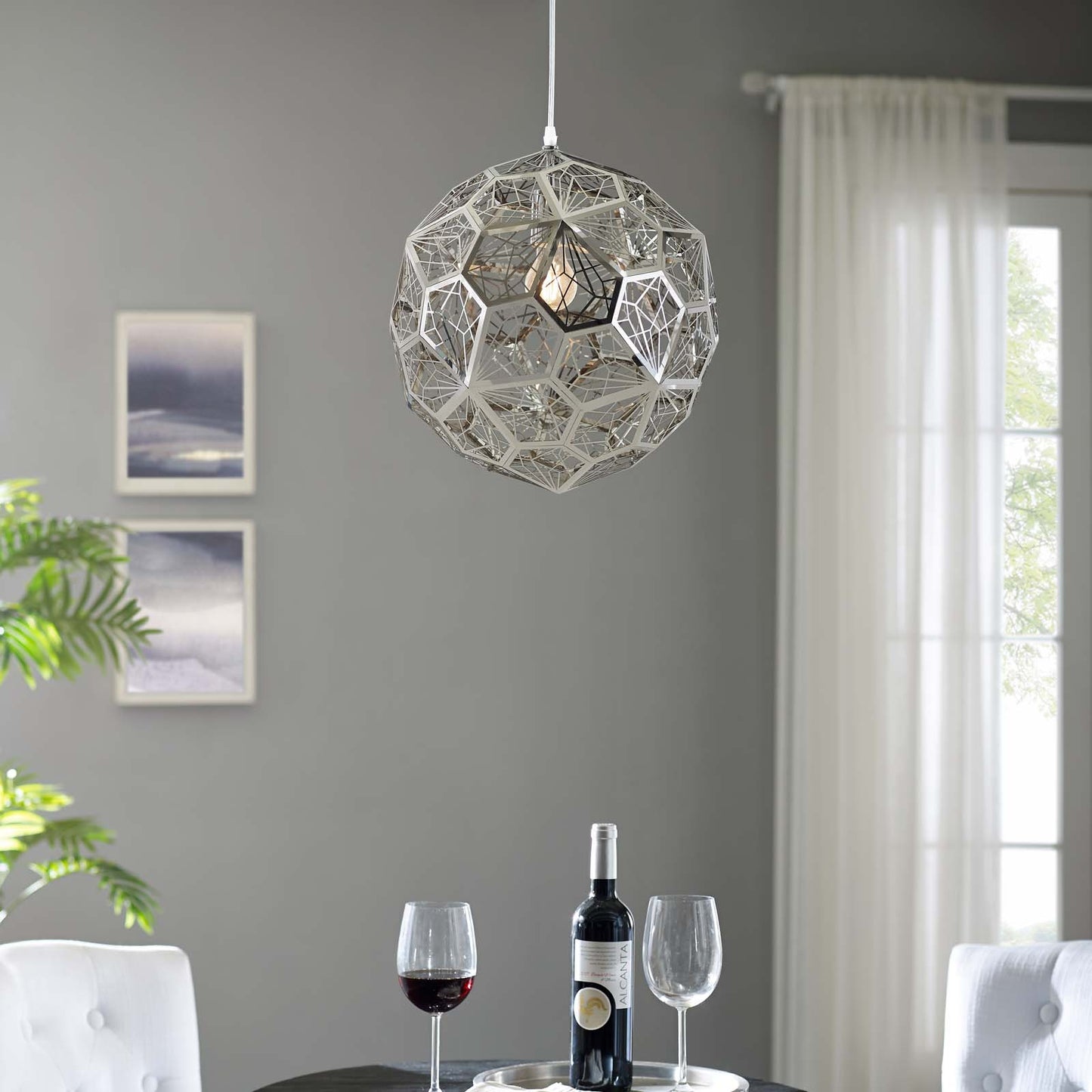 Geometric silver sphere pendant chandelier with open lattice hangs in a modern gray living room, above wine bottle & glasses.