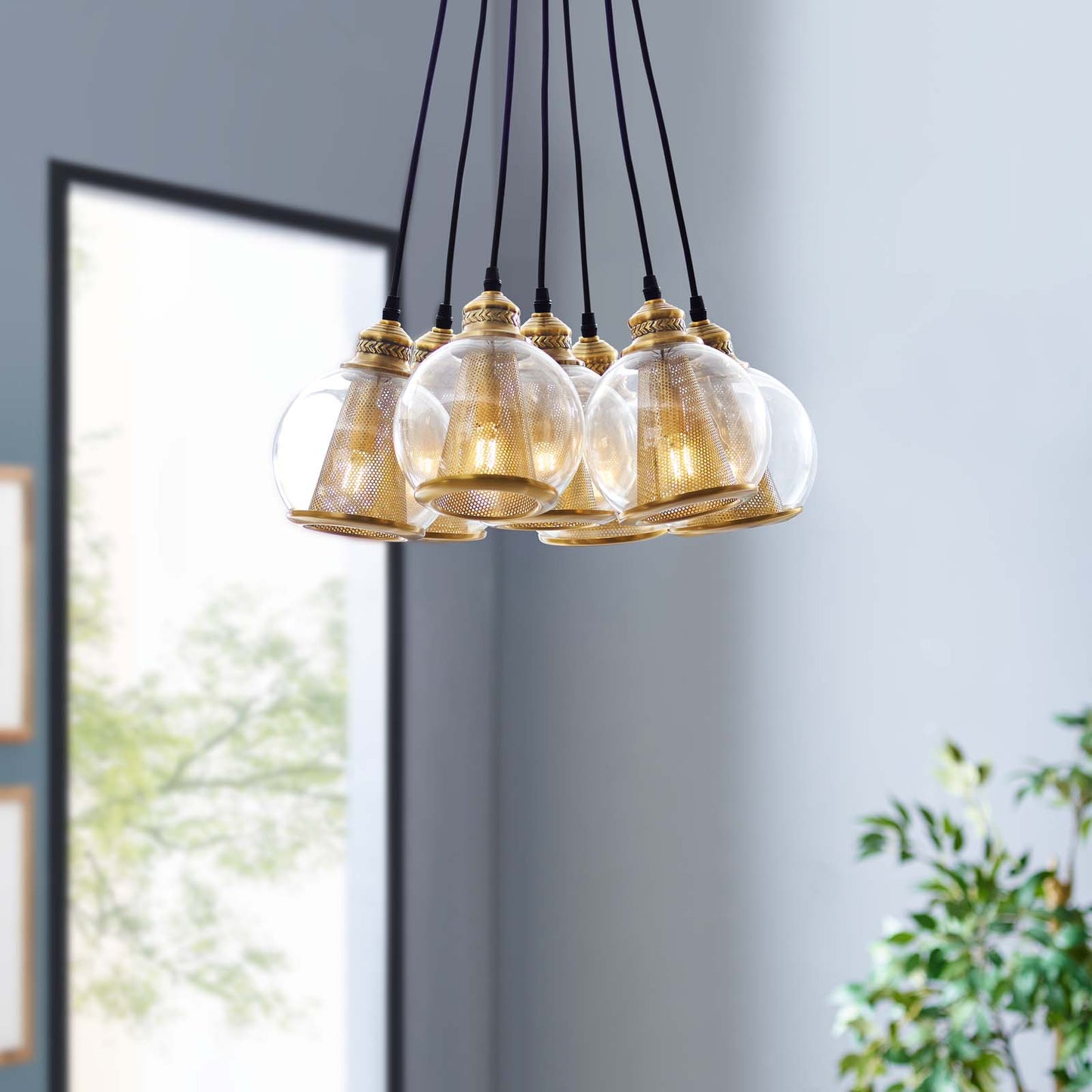 Cluster of gold-toned glass pendant lights with brass mesh cores, suspended by black cords in a modern interior.