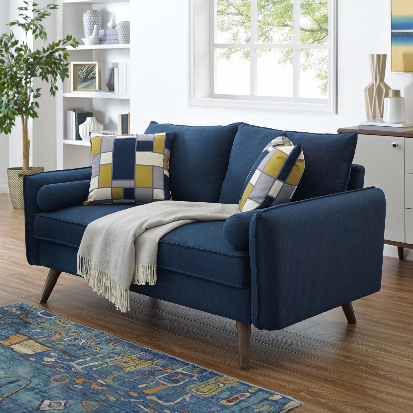 Navy-blue midcentury loveseat with slim wooden legs, plaid yellow-gray cushions, and a cream fringe throw in a bright living room