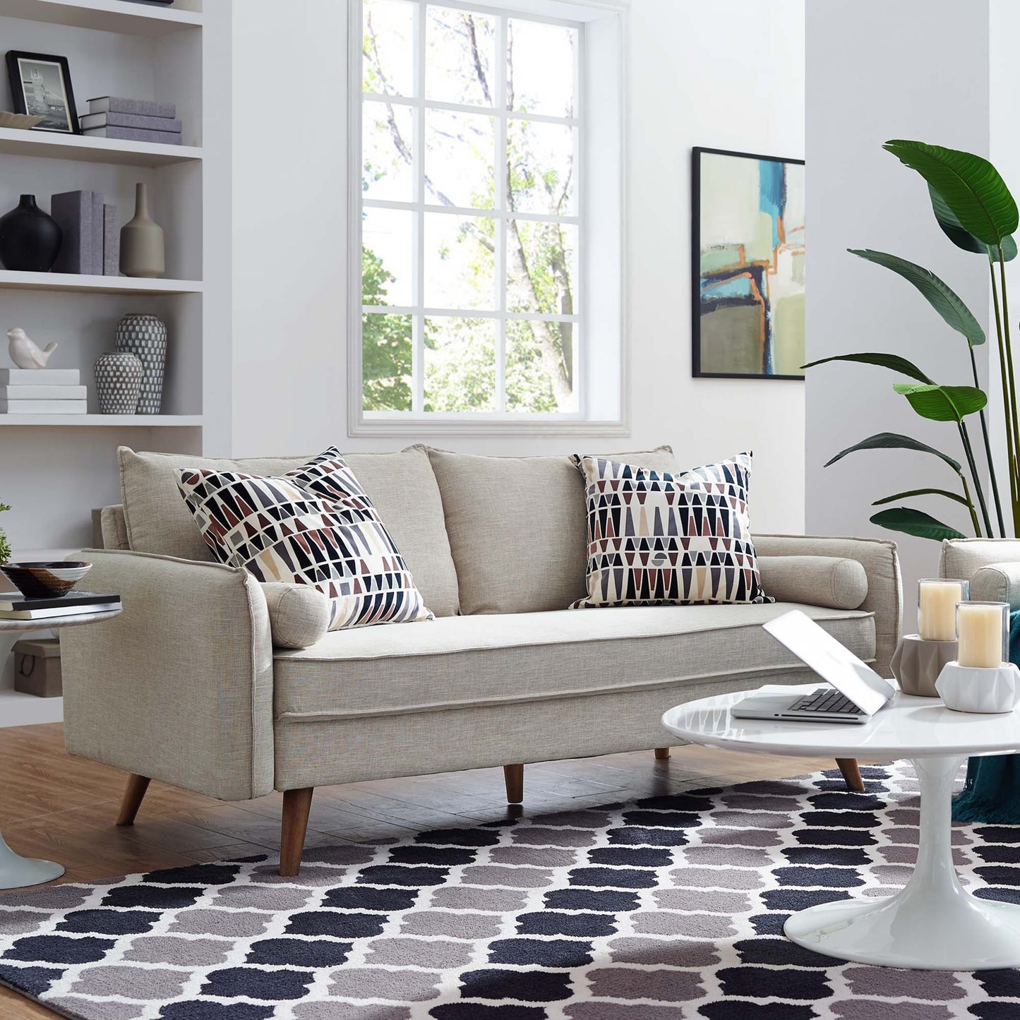 Beige fabric mid-century sofa with geometric cushions, round white coffee table, and navy rug in a bright living room.