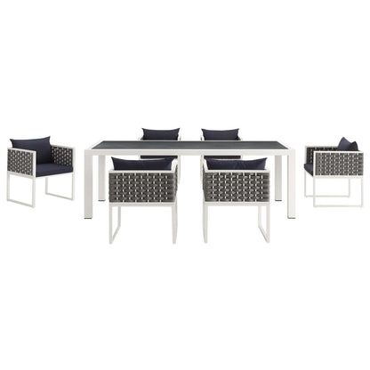 White outdoor dining table with dark top and six gray woven chairs with navy cushions.