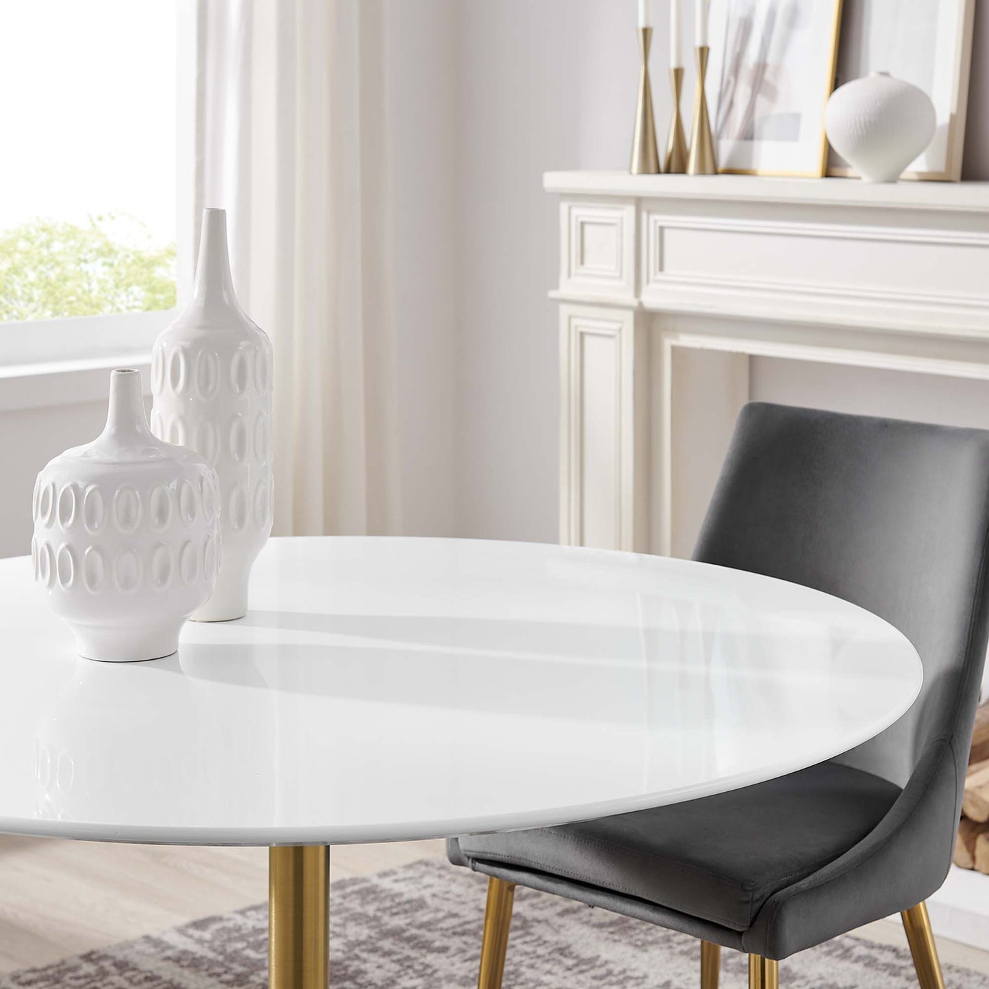 Round white wood dining table with gold legs, paired with a gray upholstered chair; two white ceramic vases on top.