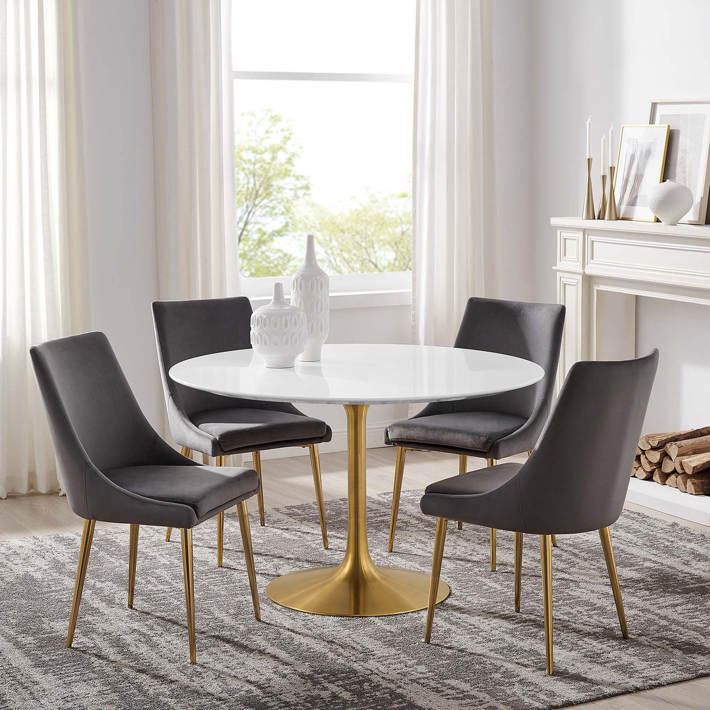 White round dining table with gold pedestal base & four gray upholstered chairs with gold legs in a bright dining room.