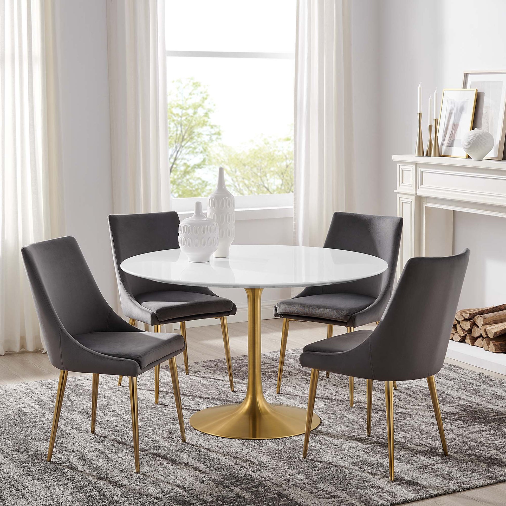 White round dining table with gold pedestal base & four gray upholstered chairs with gold legs in a bright dining room.