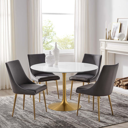 White round dining table with gold pedestal base & four gray upholstered chairs with gold legs in a bright dining room.