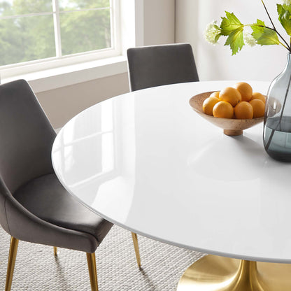 Glossy round white dining table with gold pedestal base, gray upholstered chairs, lemon bowl and vase in a bright room.