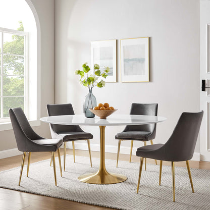 Round wood dining table with a gold pedestal, four gray chairs with gold legs, and a vase of green branches and oranges.