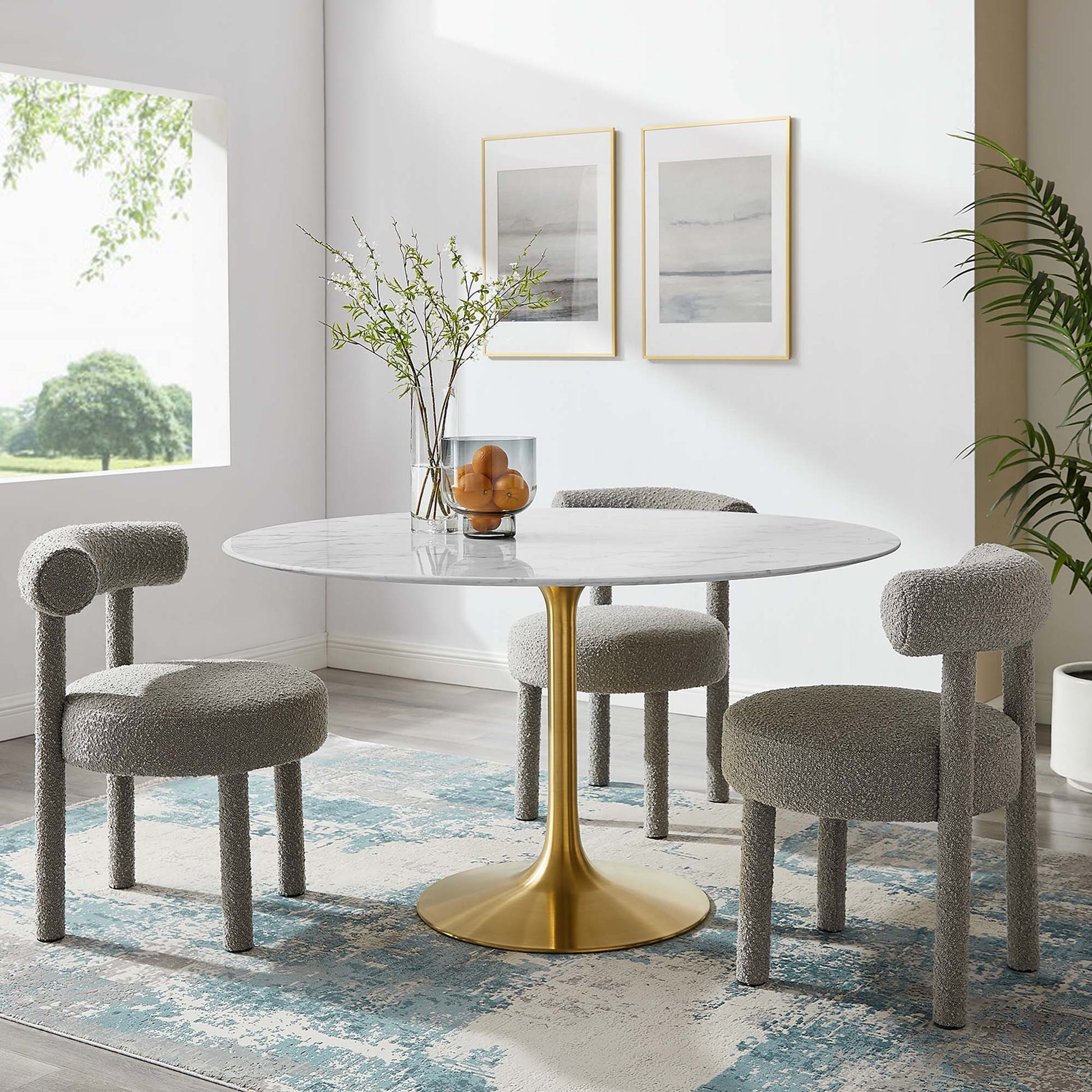 Round marble dining table with a gold pedestal base and four light gray boucle chairs in a bright modern dining room.