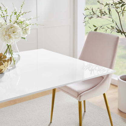 Glossy white table with gold legs, blush pink upholstered chair, vase of white flowers in bright airy dining area