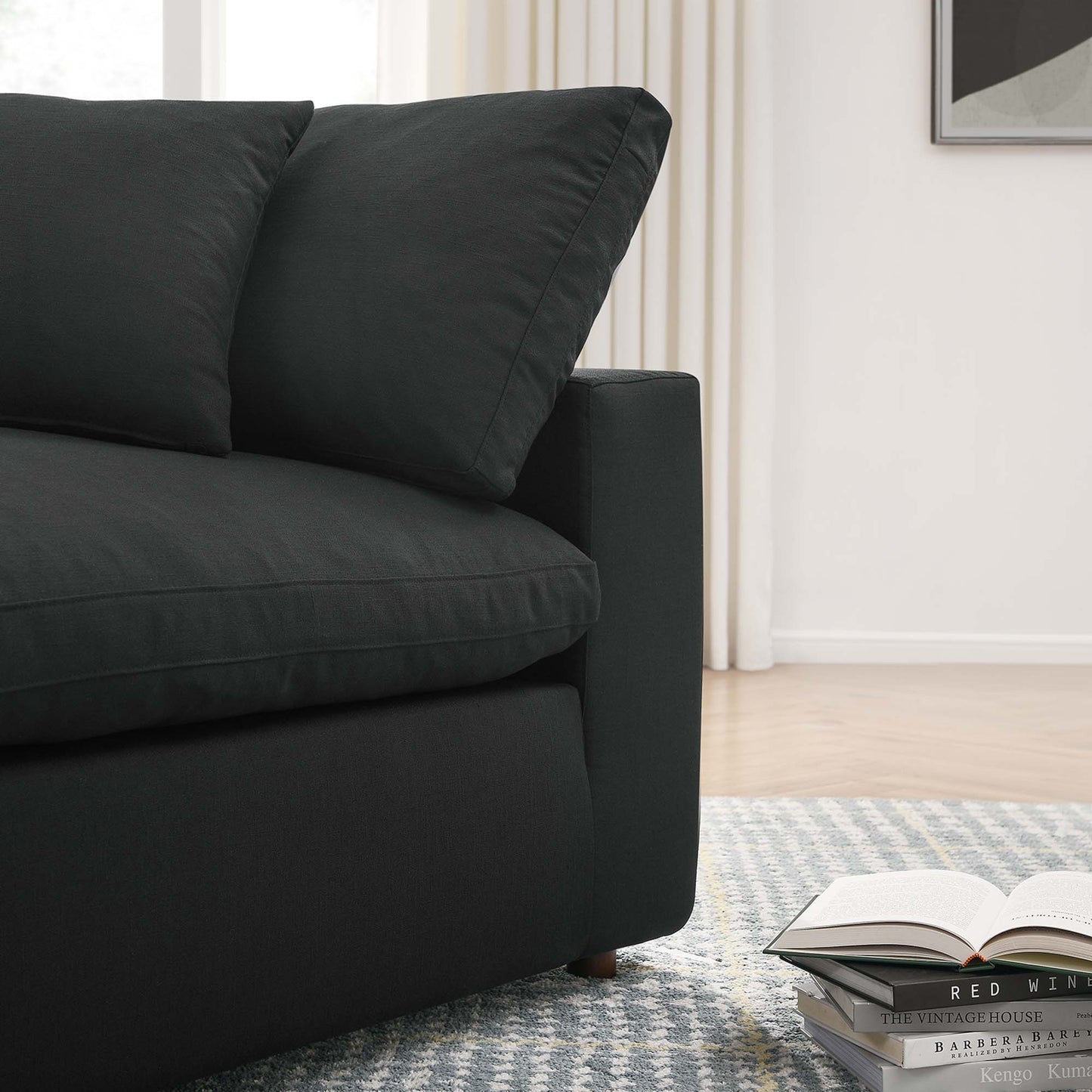 Dark charcoal fabric corner chair with two cushions in a modern living room, rug, curtains, and an open book & magazines nearby.