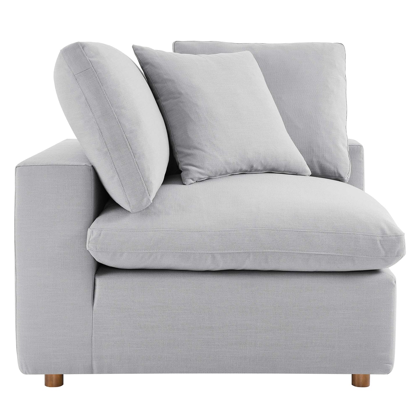 Light gray fabric corner chair with thick seat cushion, two square back pillows and a curved round bolster; wooden legs.