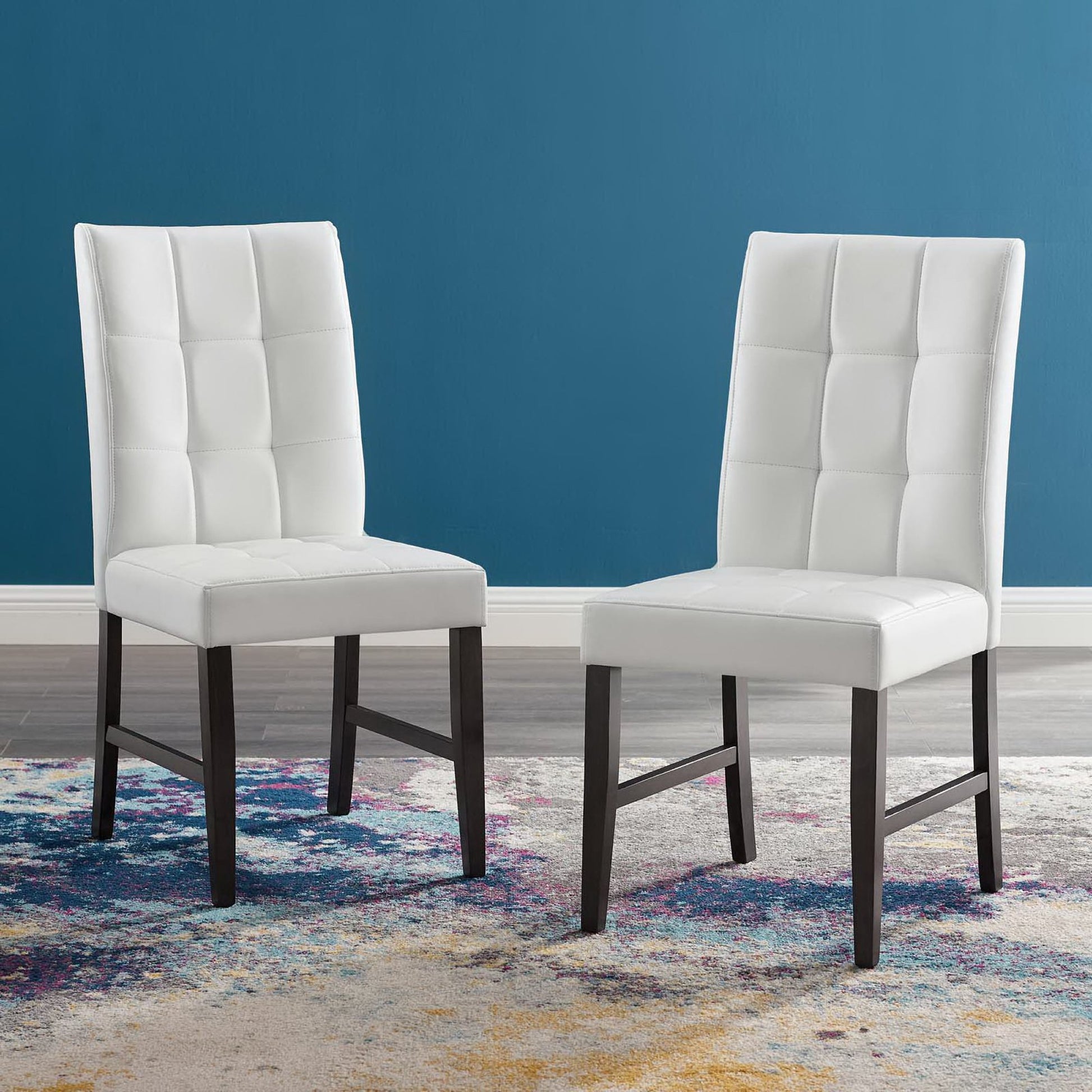 Two white tufted dining chairs with dark brown legs on a colorful patterned rug against teal walls.