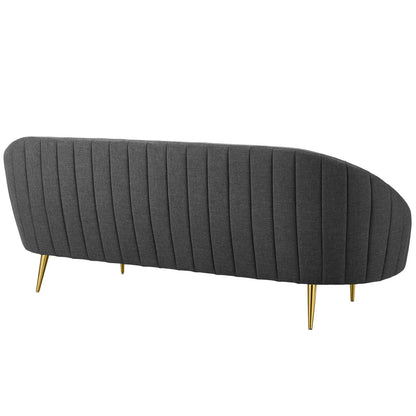Gray curved sofa with vertical channel tufting and gold tapered legs, mid-century modern style.