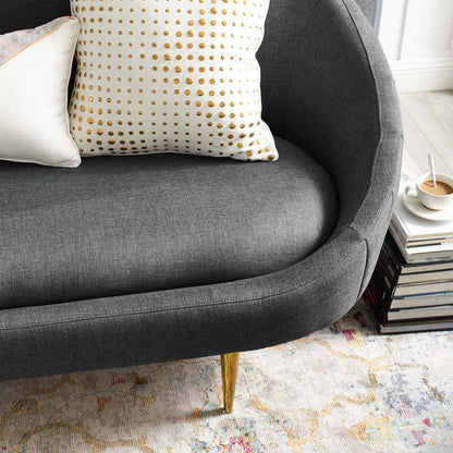 Dark gray curved sofa with gold legs, white polka-dot pillow, alongside a stack of books and a coffee cup.