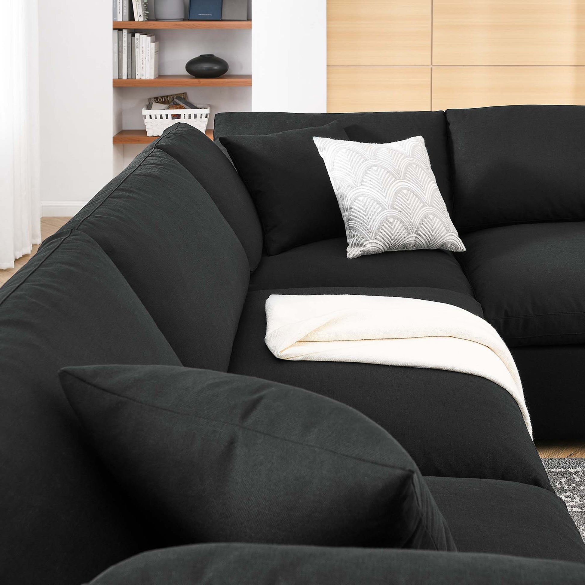 Black sectional sofa with a white throw blanket and a patterned white pillow in a modern living room.