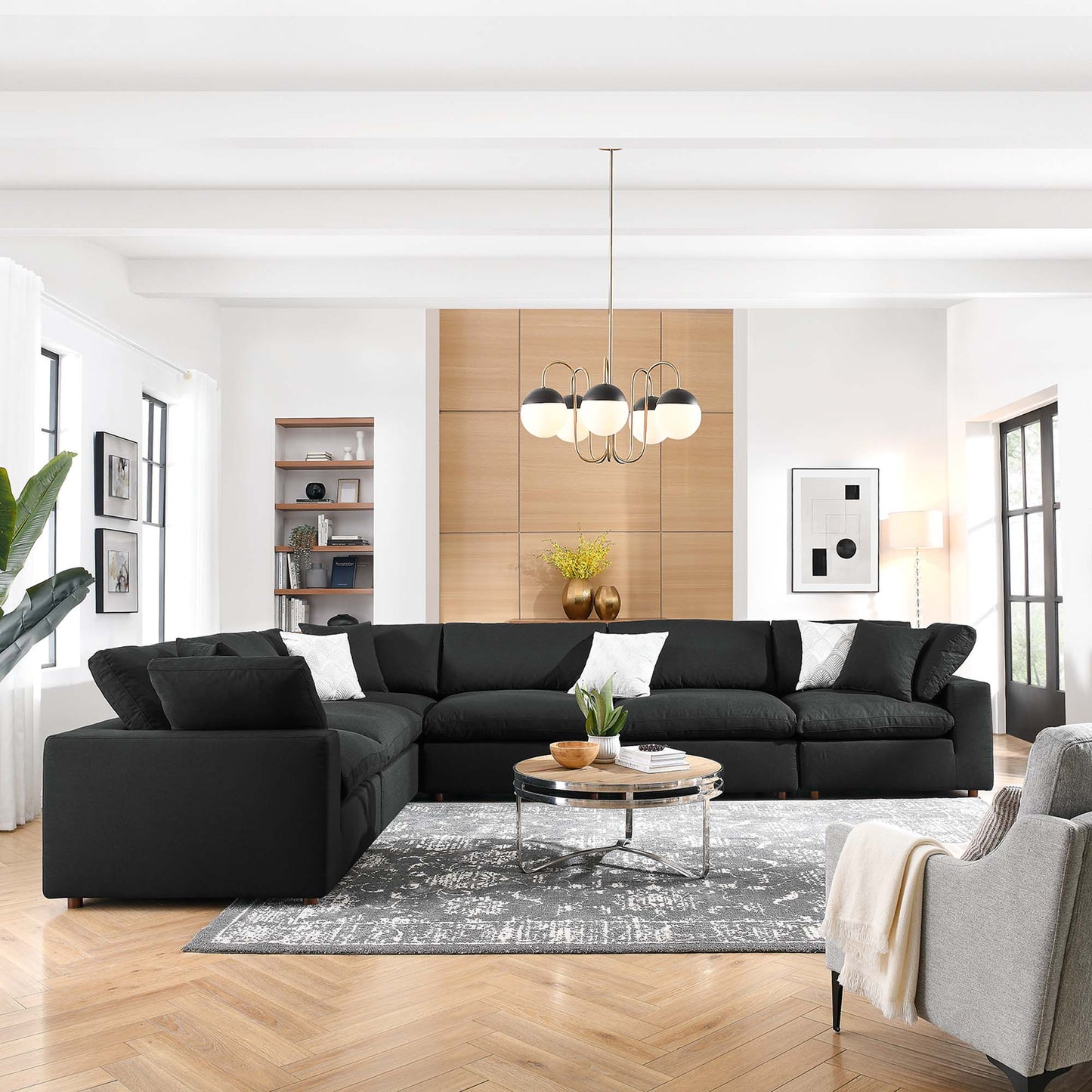 L-shaped black sectional sofa set in a bright modern living room with a round glass coffee table, gray rug and wood floors.
