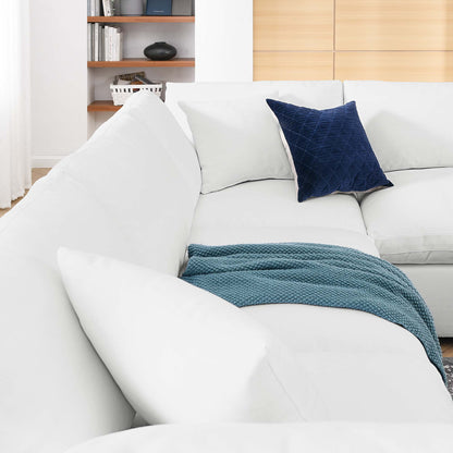 White sectional sofa with teal knitted throw and navy square cushion in a bright living room.