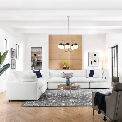Bright modern living room with white sectional, navy pillows, round glass coffee table, gray rug, wood cabinet, chandelier.