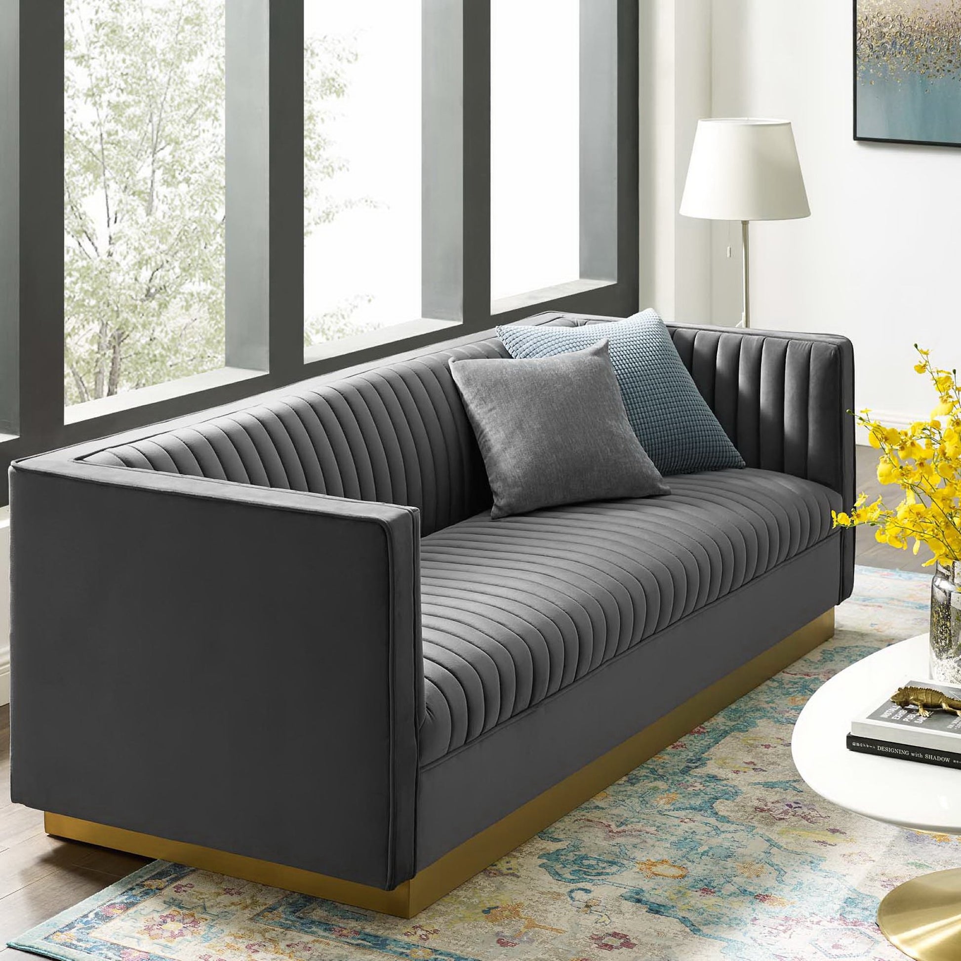Gray vertical-channel tufted velvet sofa with a wooden base in a modern living room.