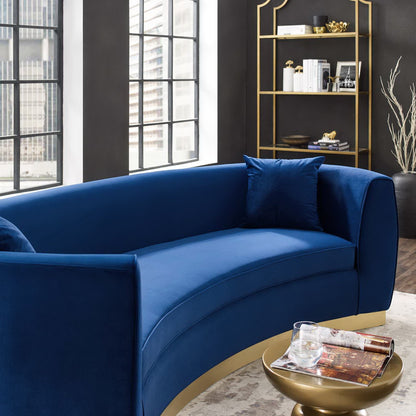 Curved navy velvet sofa with gold base and cushions in a modern living room, round gold coffee table with magazines.