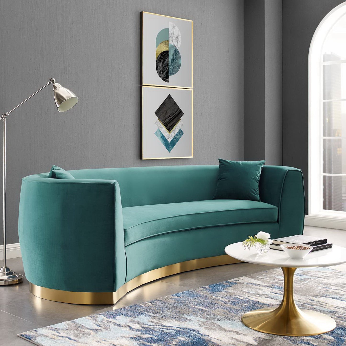 Blue velvet curved sofa with a gold metal base and matching cushions in a modern living room.