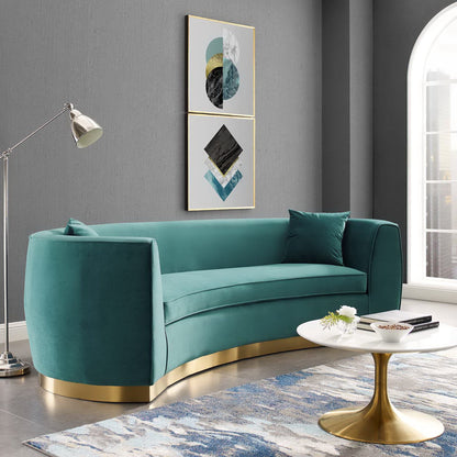 Blue velvet curved sofa with a gold metal base and matching cushions in a modern living room.