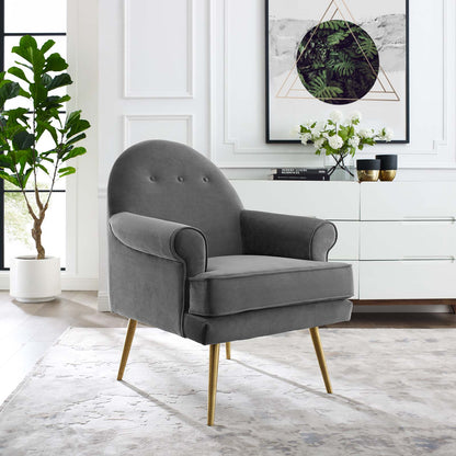 Gray velvet upholstered armchair with tufted back, curved arms and gold tapered wooden legs, in a modern living room.