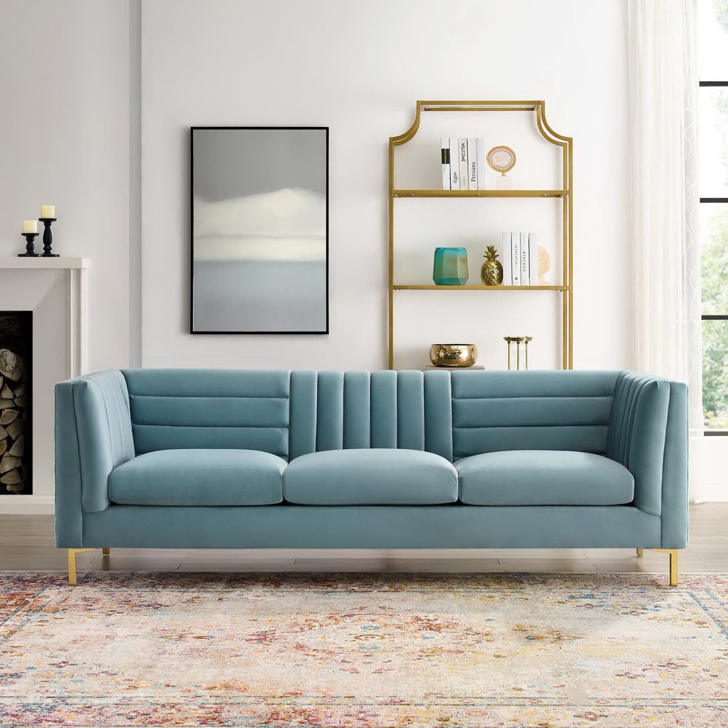 Blue tufted velvet sofa with gold metal legs in a bright living room; arched gold bookshelf, abstract rug, & framed art.