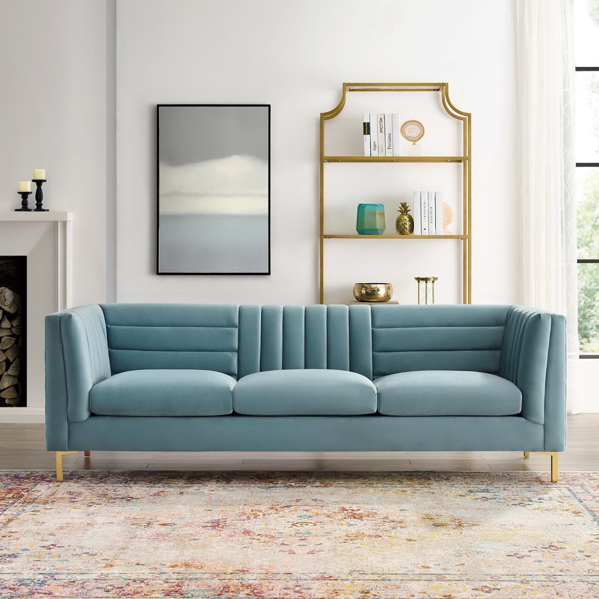 Blue tufted velvet sofa with gold metal legs in a bright living room; arched gold bookshelf, abstract rug, & framed art.