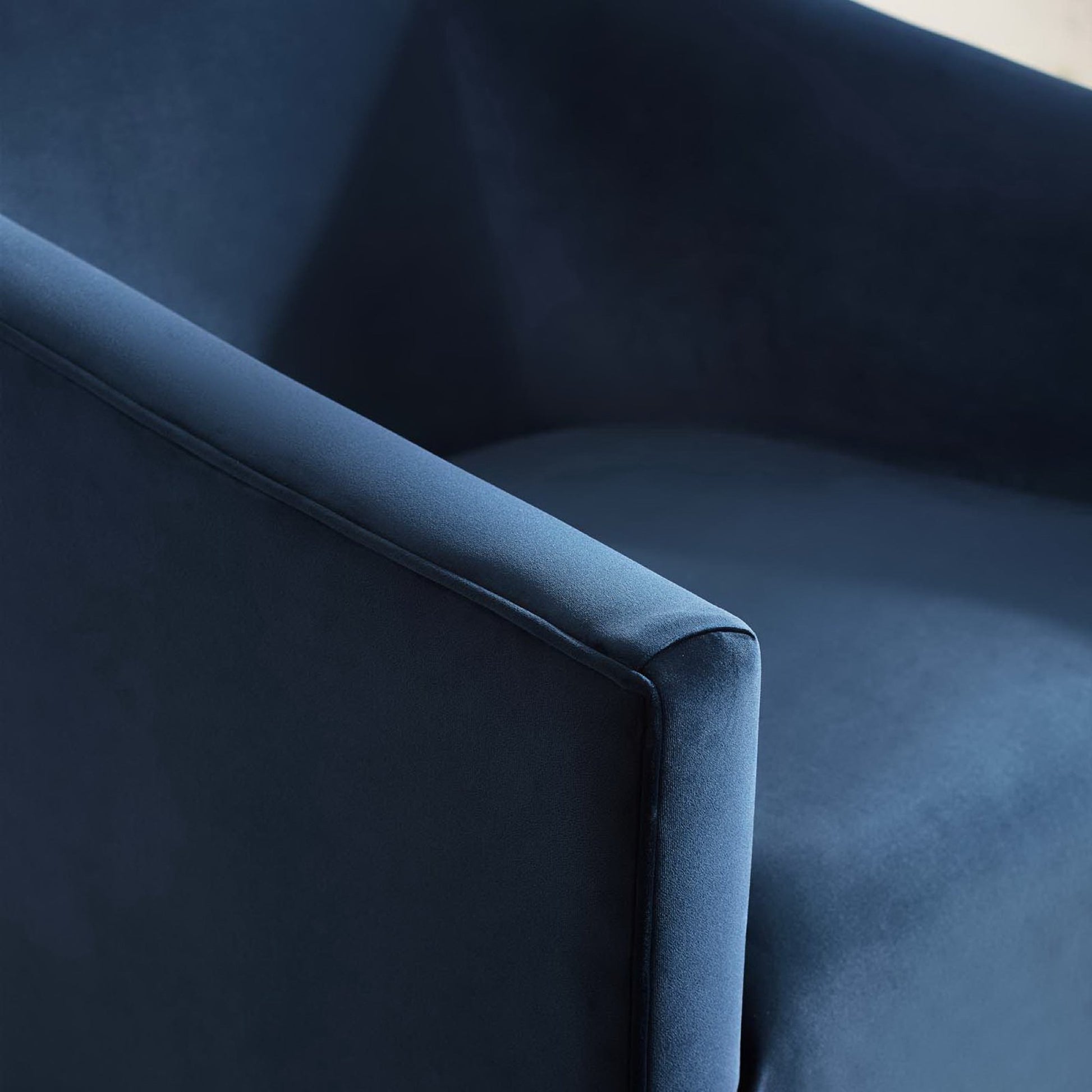 Navy blue velvet armchair close-up with curved armrest and seating, modern style.