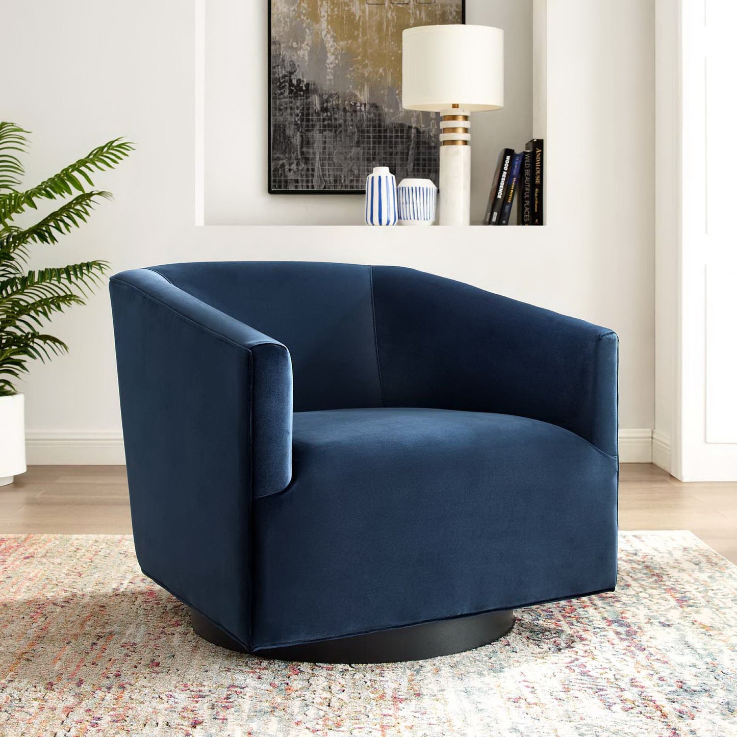 Deep blue velvet swivel chair with curved arms on a round black pedestal base; modern accent seating.