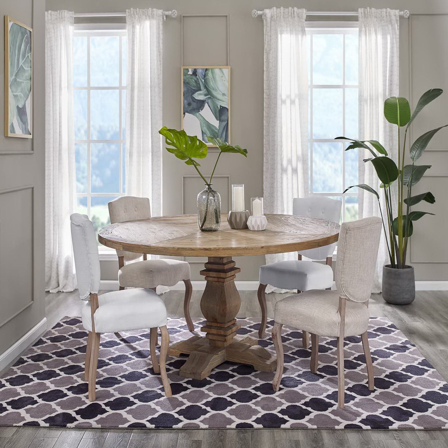 Round pine wood pedestal dining table with beige upholstered chairs; purple geometric trellis rug, leafy plants, and light gray walls.