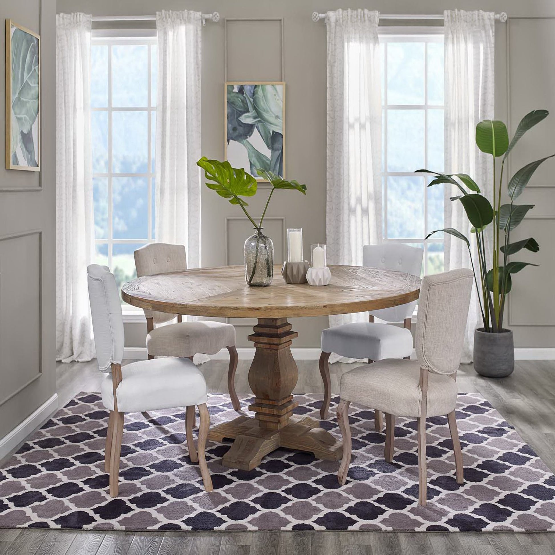 Round pine wood pedestal dining table with beige upholstered chairs; purple geometric trellis rug, leafy plants, and light gray walls.