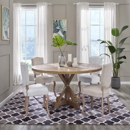 Round wooden dining table with pedestal base, beige upholstered chairs, neutral room with sheer curtains and plants; purple lattice rug.