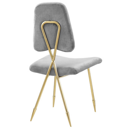 Grey velvet dining chair with gold metal X-frame legs and curved backrest.