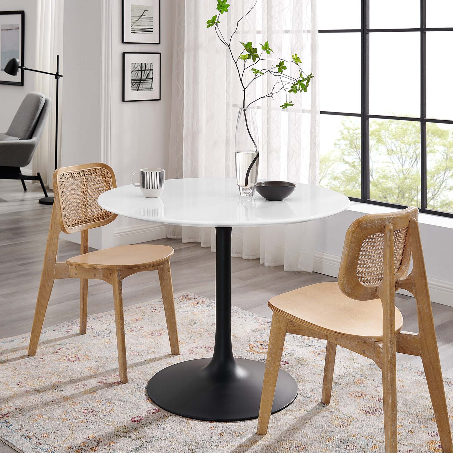 Round wood dining table with a black pedestal base, flanked by natural wood chairs with cane backs; modern Scandinavian dining set.