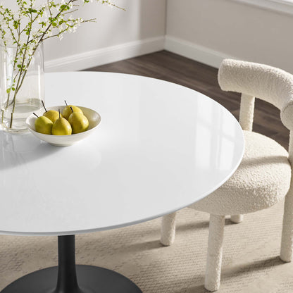 Round wood dining table (48-inch) in a bright room, with a bowl of pears, a glass vase with branches, and a cream boucle chair.