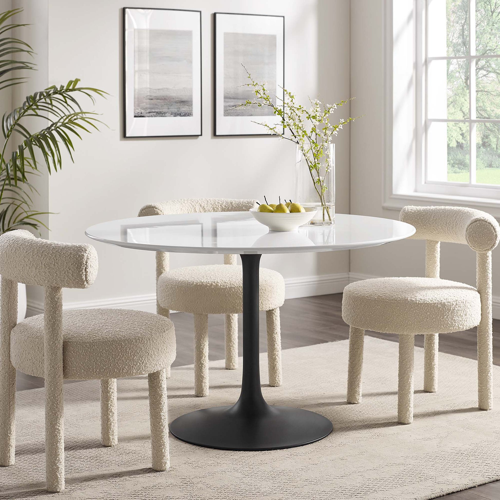 Round wood dining table on a black pedestal base with four cream boucle dining chairs in a bright modern dining nook.