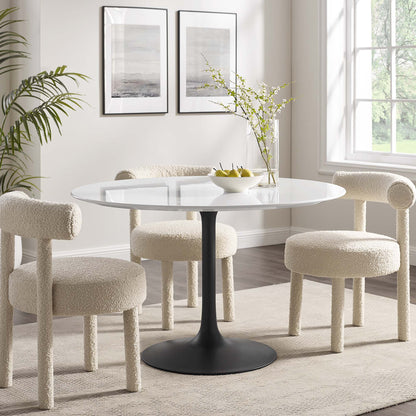 Round wood dining table on a black pedestal base with four cream boucle dining chairs in a bright modern dining nook.
