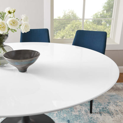 Round wood dining table in white finish with a dark ceramic bowl, vase of white flowers, blue upholstered chairs, and a bright window view.