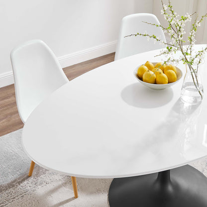 Oval wood dining table with a black pedestal base, white molded chairs, a lemon bowl and a vase with branches.